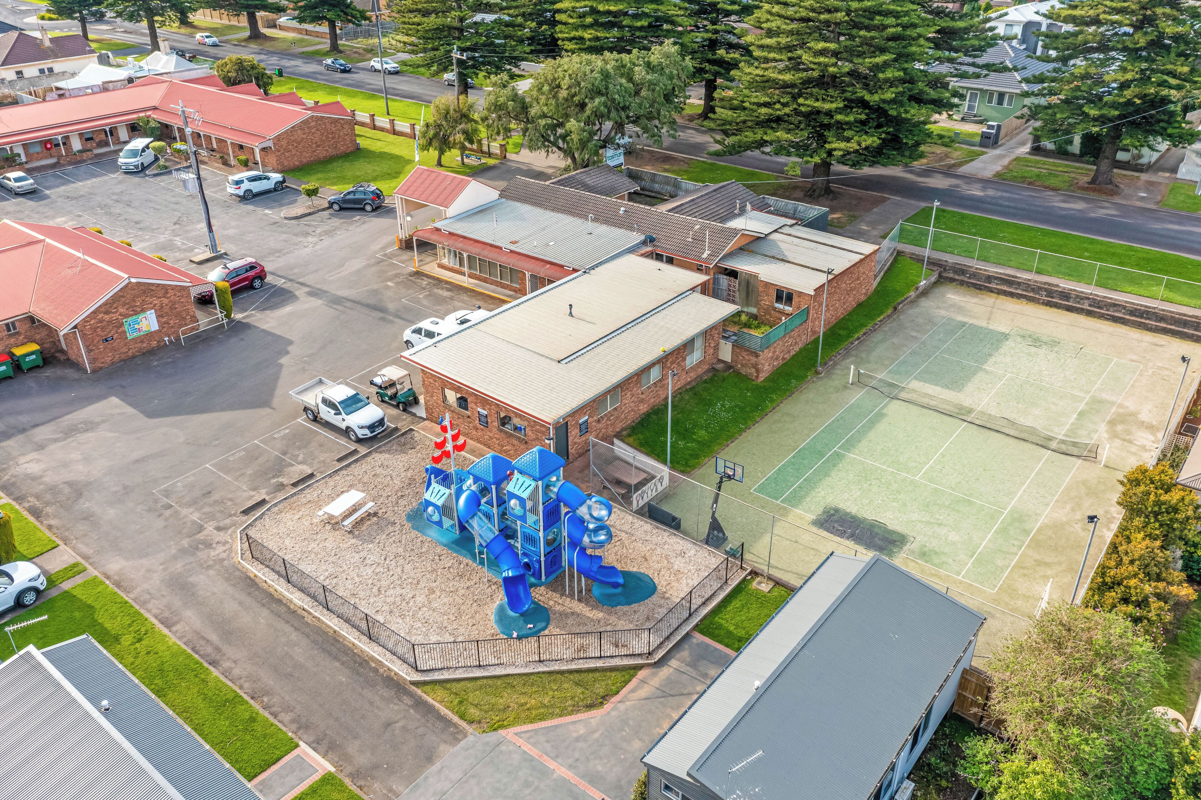 An aerial view of a school with a playground, a tennis court, and a parking lot.