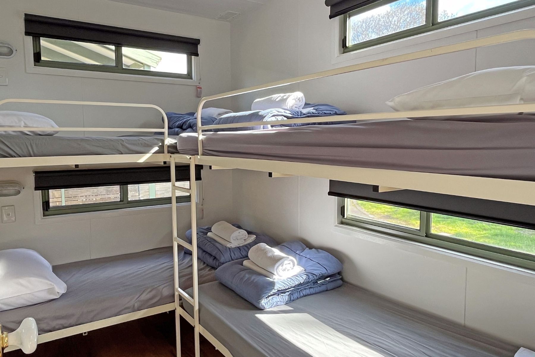 A bunk bed room with two windows, each with a black blind. There are pillows and blankets on the beds.