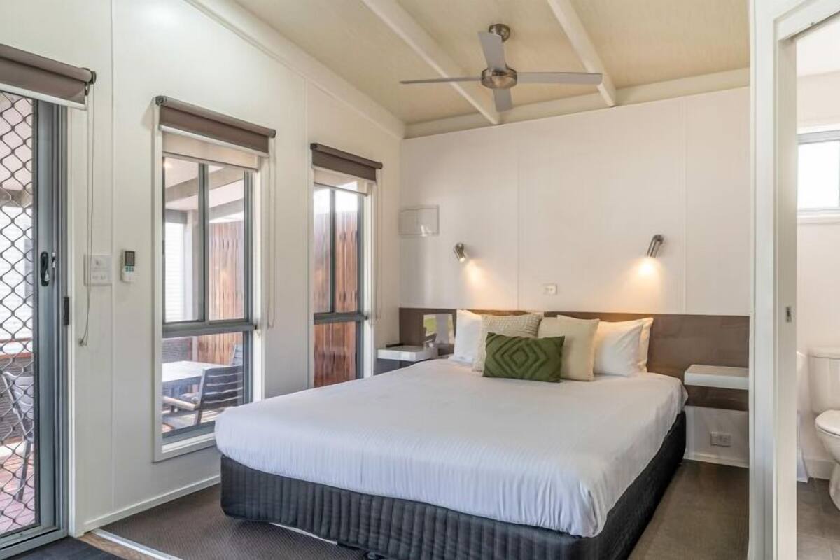 A bedroom with a bed, bedside tables, a ceiling fan, and a toilet.