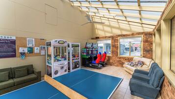 Relax in this spacious room with a ping pong table, green sofa, and blue armchair. Enjoy the view from the window and unwind with a ceiling fan above.
