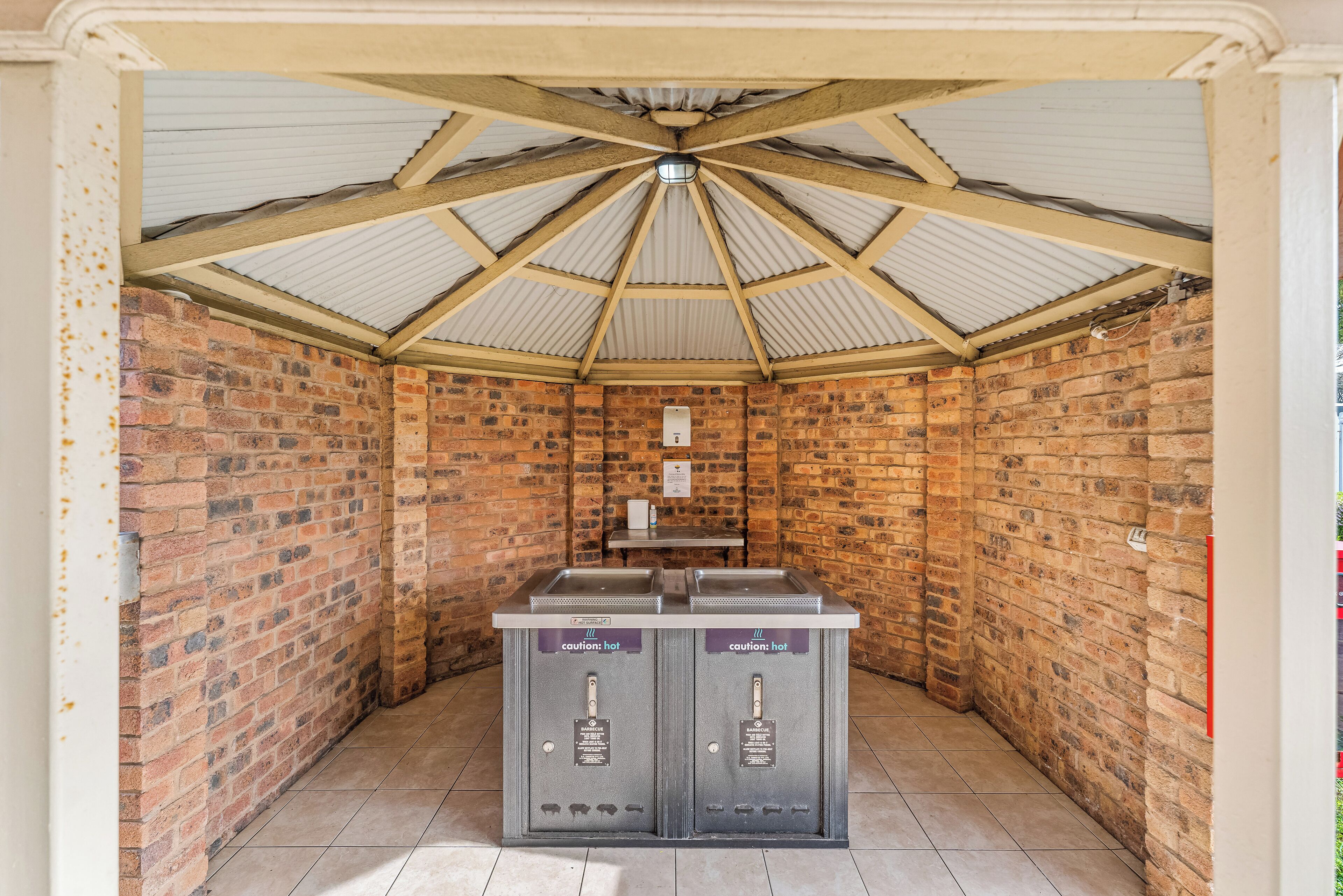 A covered outdoor area with a brick wall, a metal roof, and two caution signs on a metal counter.