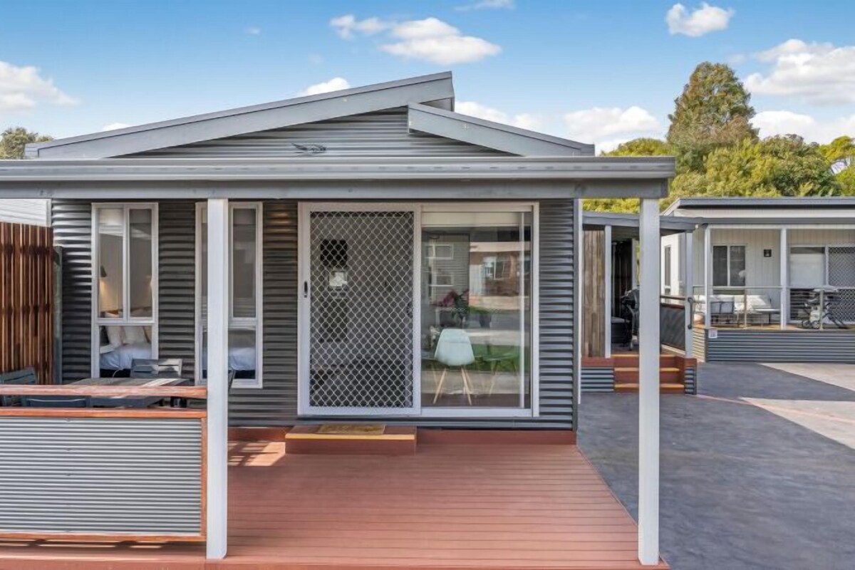 A modern RV-style accommodation with a covered patio, a fenced outdoor area, and a sliding glass door entrance.