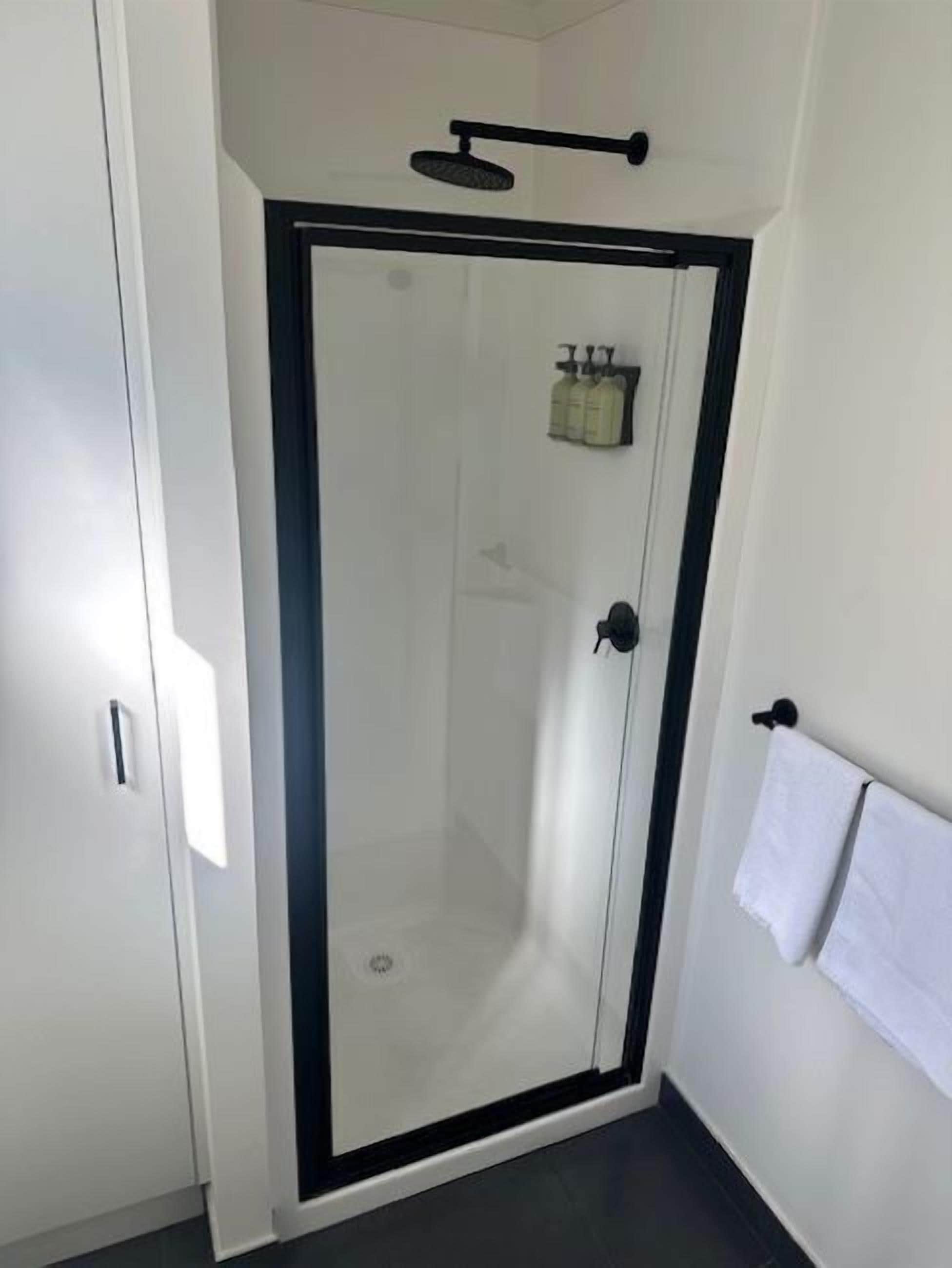 A modern bathroom with a glass-enclosed shower, a towel rack, and a small shelf with toiletries.