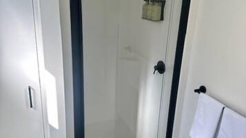 A modern bathroom with a glass-enclosed shower, a towel rack, and a small shelf with toiletries.