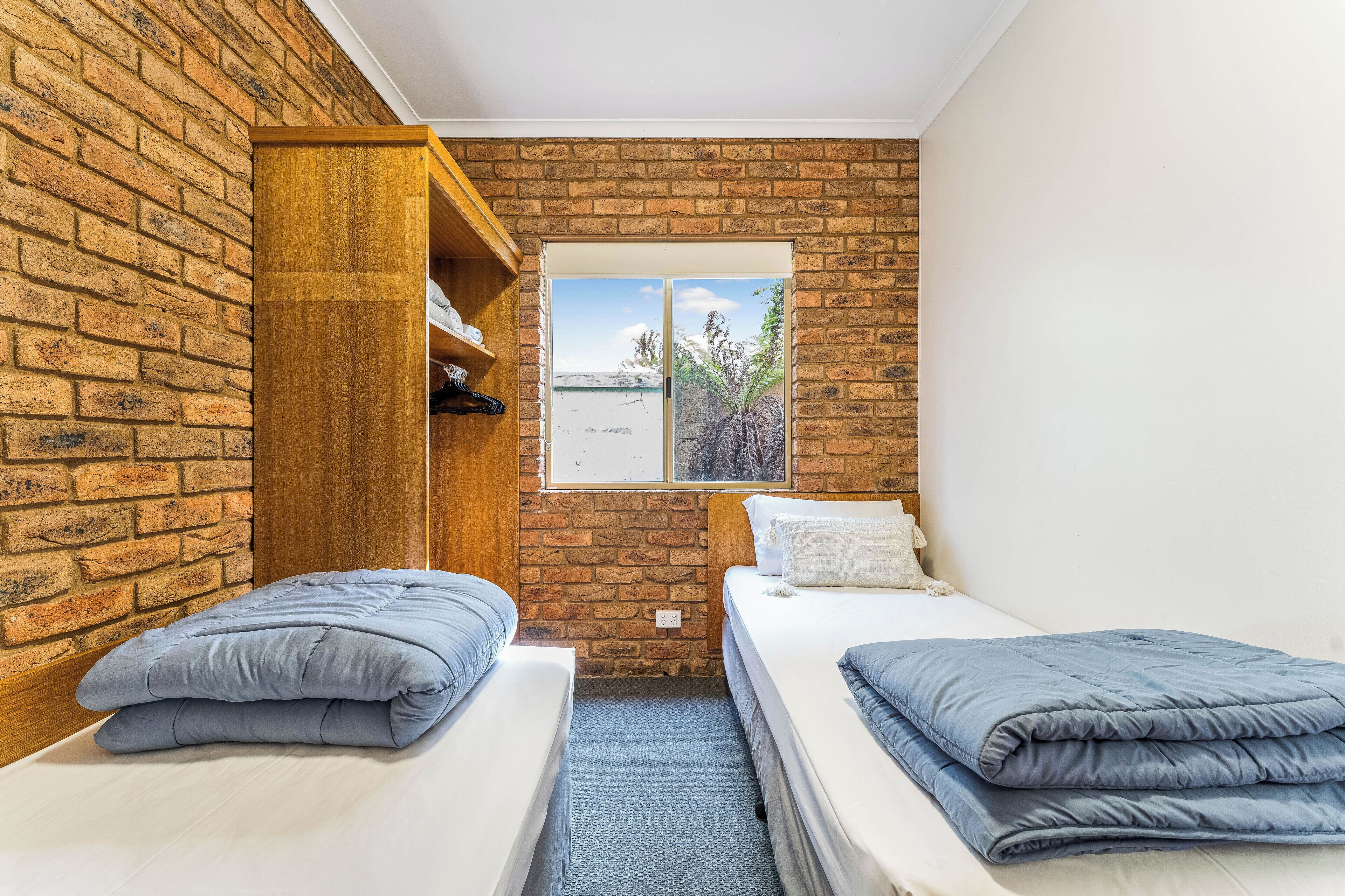 A room with two beds, a wooden wardrobe, and a window with a view of trees.
