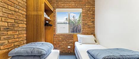 A room with two beds, a wooden wardrobe, and a window with a view of trees.
