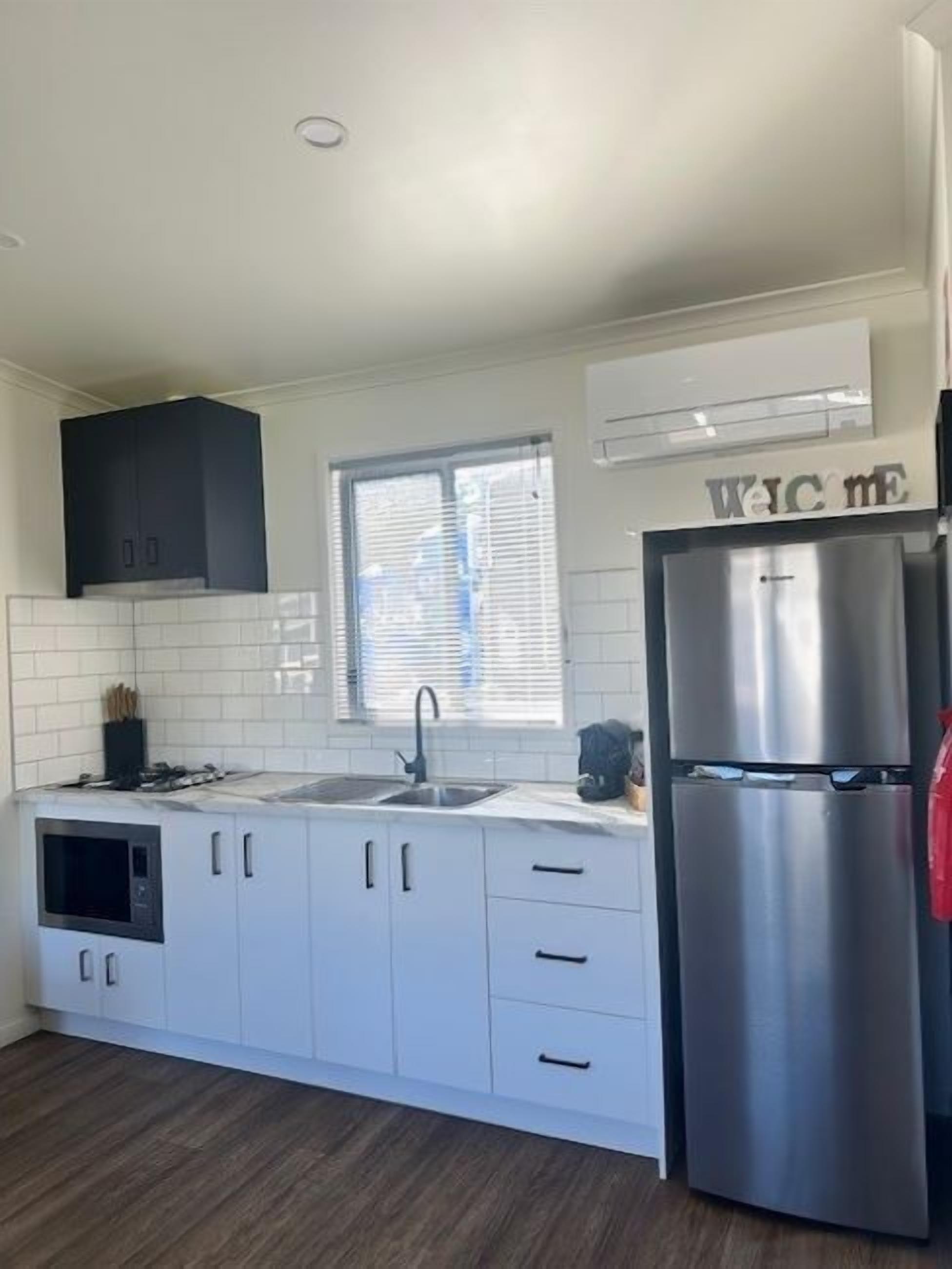 Una cocina moderna con armarios blancos, un refrigerador de acero inoxidable y una ventana con persianas.