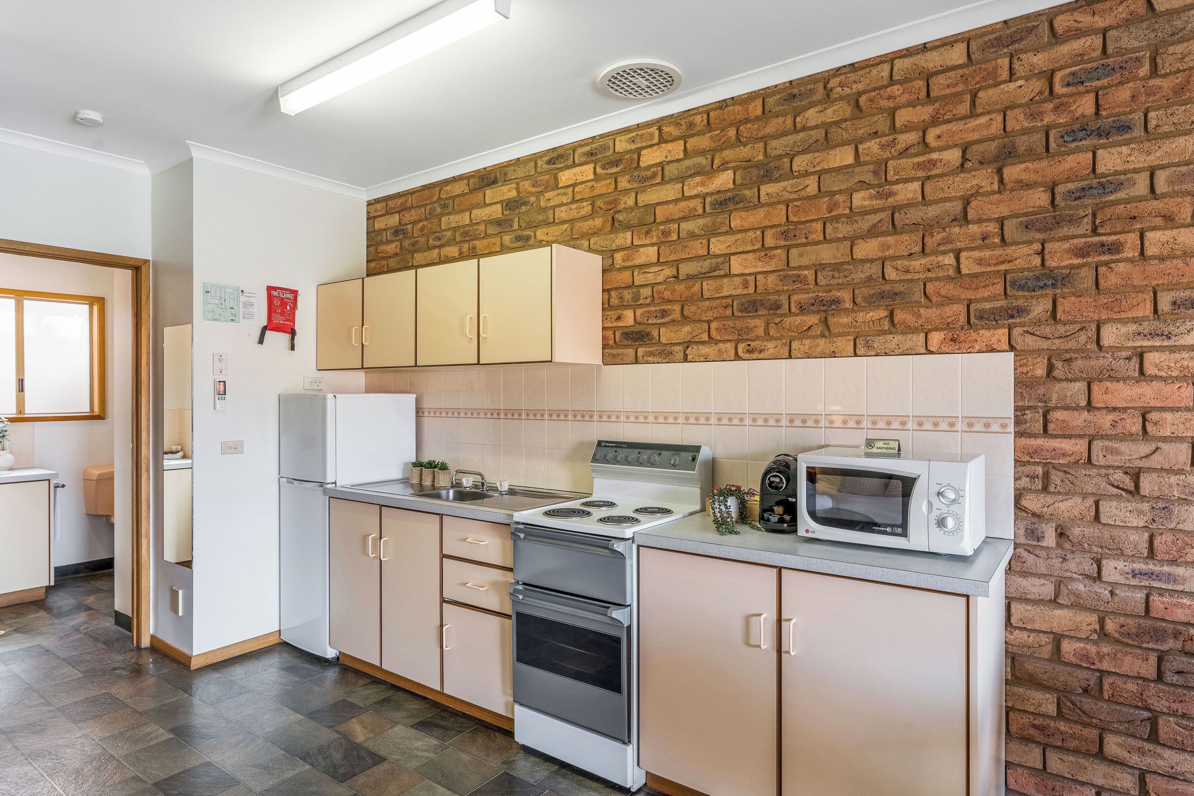 Cozinha com parede de tijolos, armários brancos, fogão e micro-ondas.