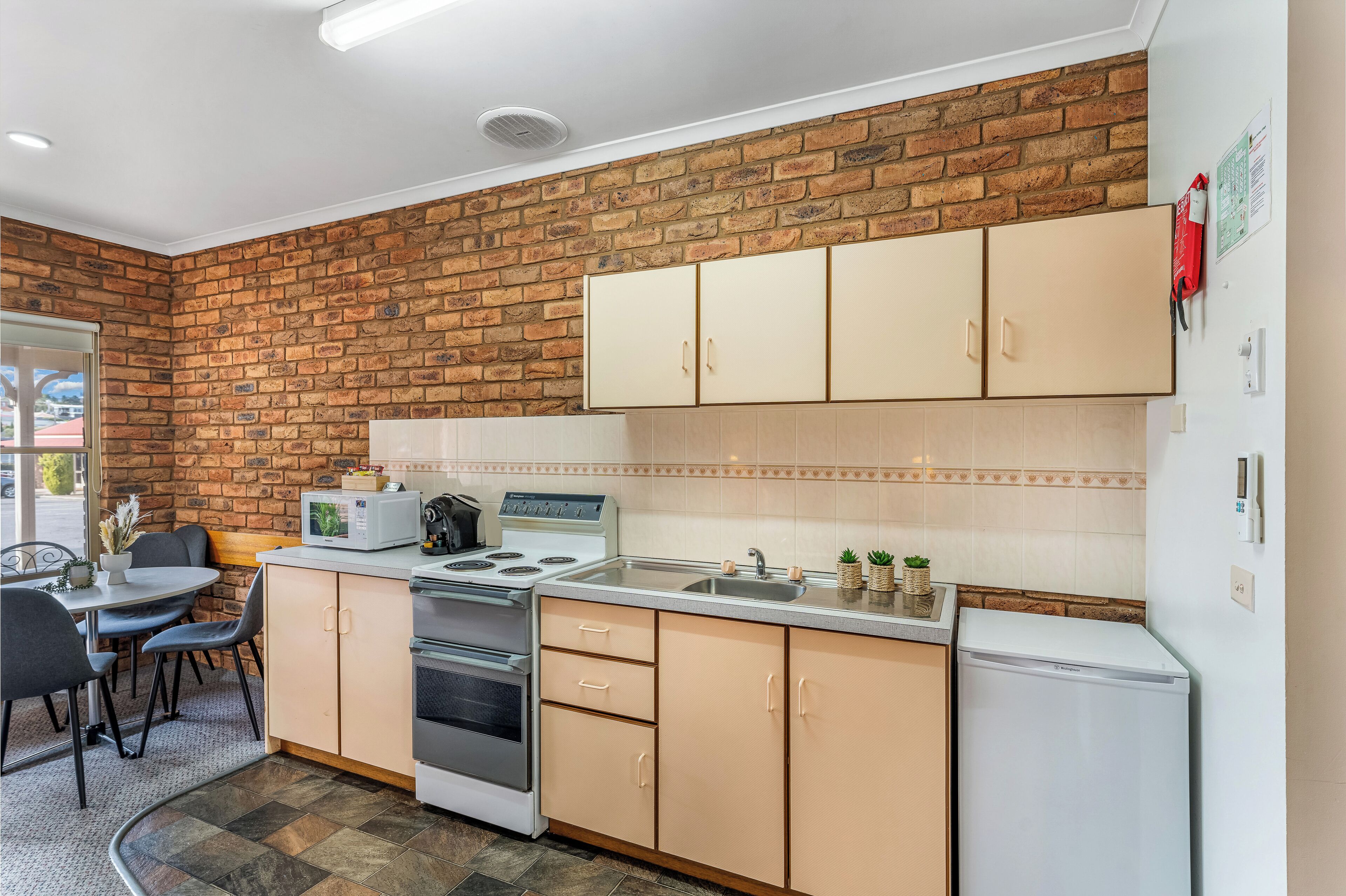Una cocina compacta con pared de ladrillo, un comedor con mesa y sillas, y un refrigerador.