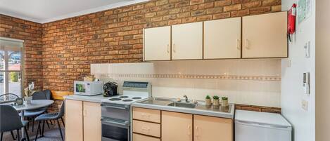 Una cocina compacta con pared de ladrillo, un comedor con mesa y sillas, y un refrigerador.