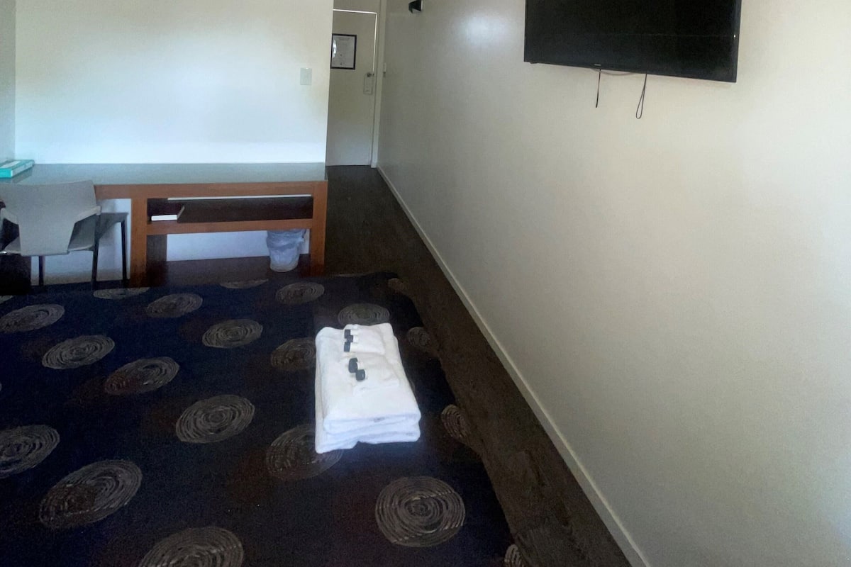 Ein Zimmer mit flachbildschirm-Fernseher an der Wand, einer Bank, einem Stuhl und einem gemusterten Teppich.