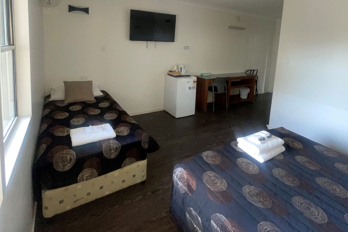 Ein Zimmer mit zwei Betten, einem Schreibtisch, einem kleinen Kühlschrank und einem Fernseher an der Wand.