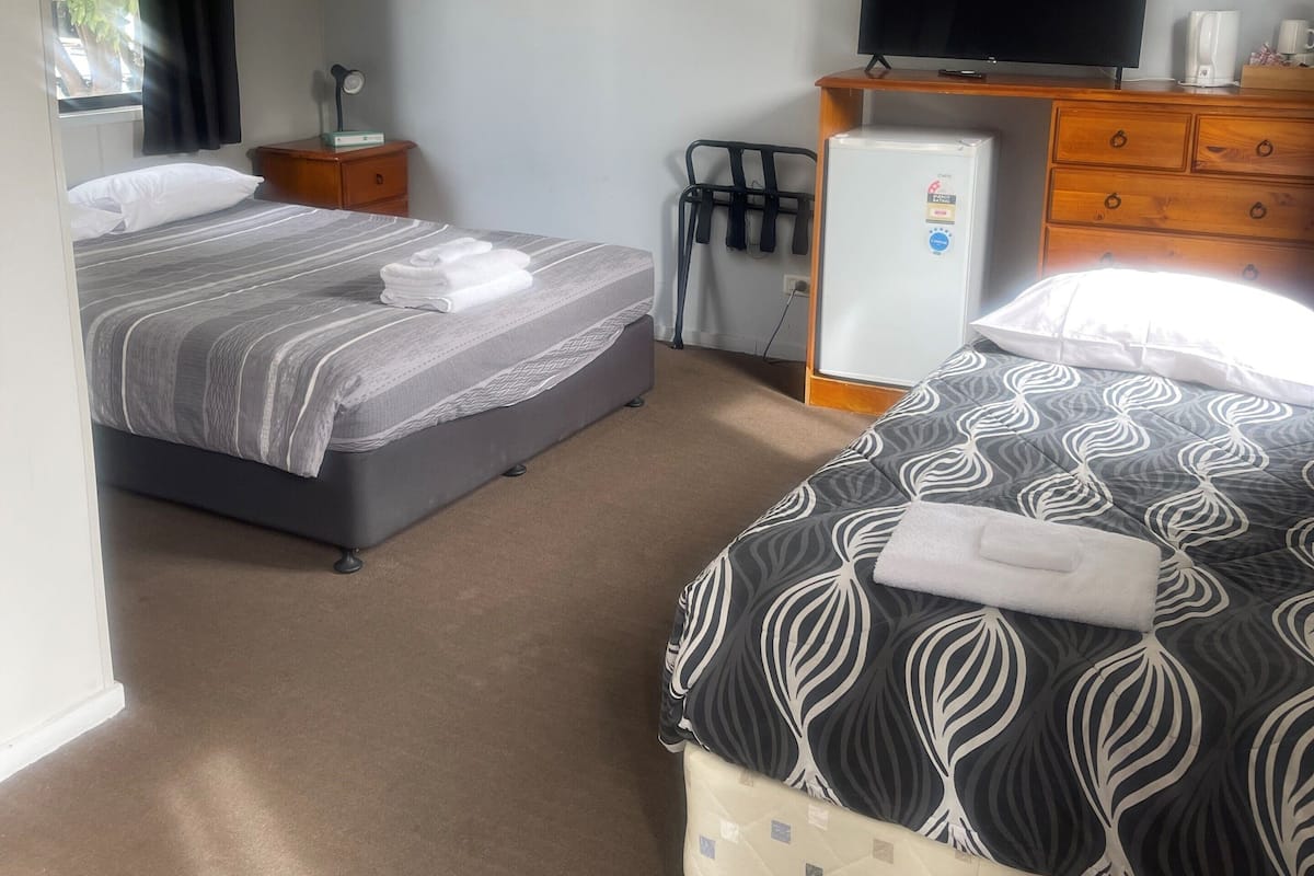 Ein Hotelzimmer mit zwei Betten, einem Fernseher, einem Kühlschrank, einem Schreibtisch und einem Stuhl.