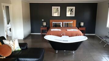 A modern bedroom with a large black bathtub, a wooden bed with two pillows, and a nightstand with a lamp.