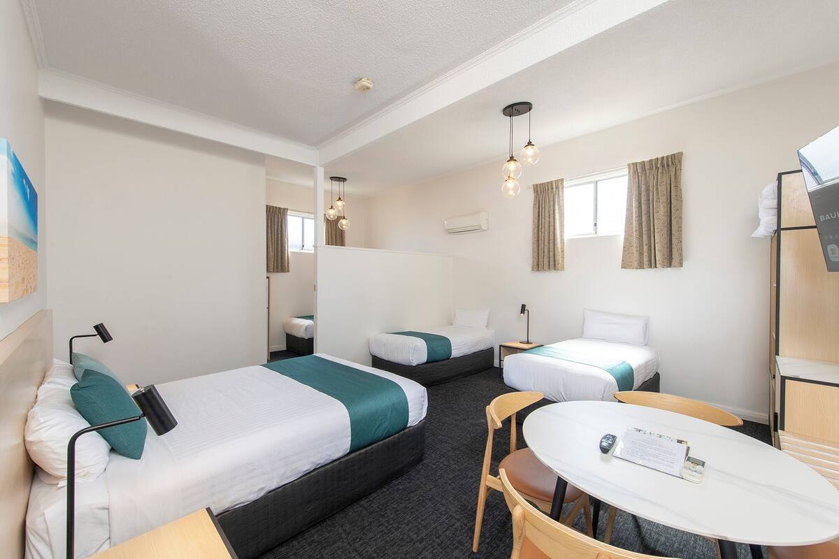 A hotel room with two beds, a small table, a chair, and a desk with a computer.