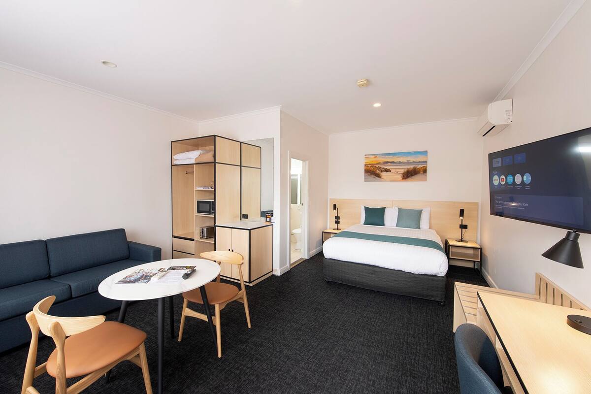 A hotel room with a bed, a sofa, a desk, a chair, a TV, and a wardrobe.