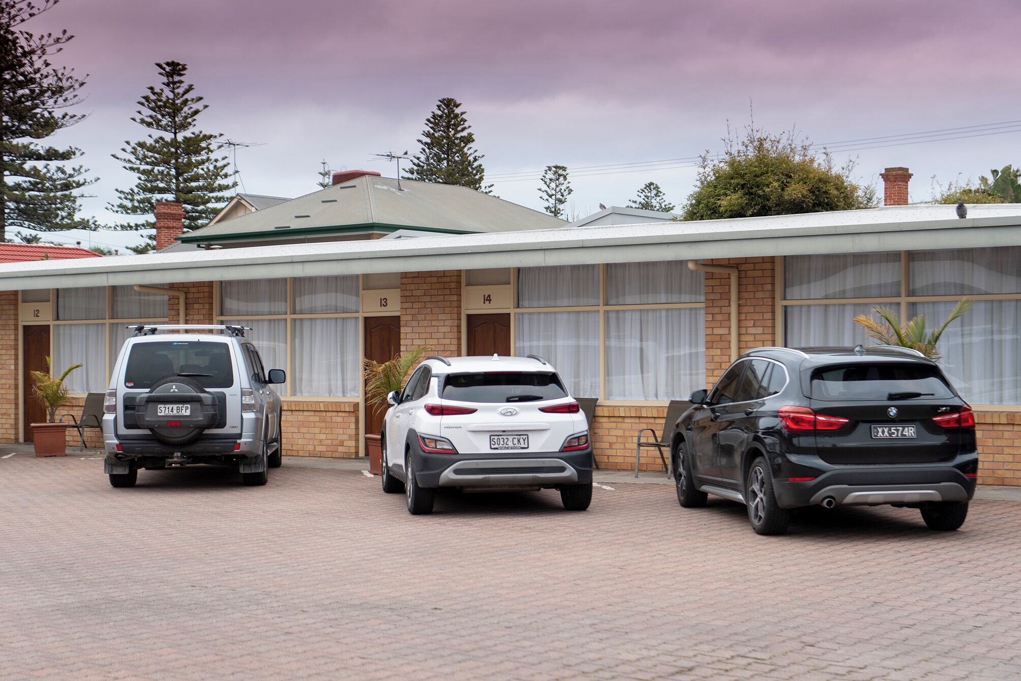 Three cars parked in front of a building with numbered doors and a brick facade.