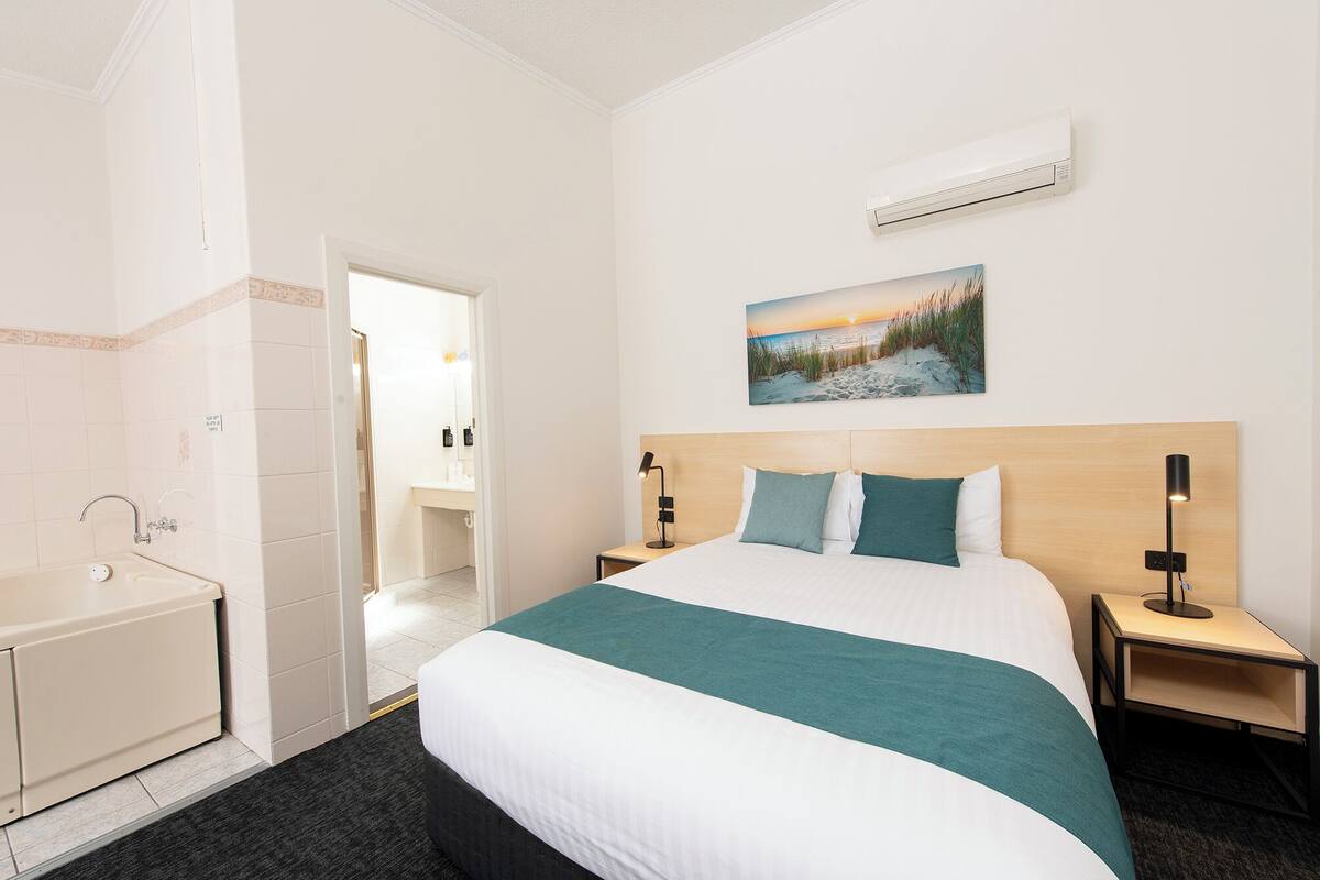 A hotel room with a large bed, a painting of a beach scene, a bathtub, and a wooden headboard.