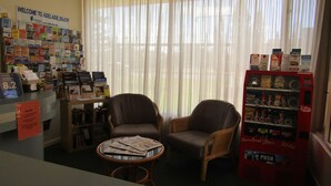 A room with a reception desk, a wall of books, two chairs, a small table with newspapers, and a vending machine. - Glenelg Motel (Glenelg North)