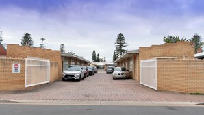 A parking area with multiple cars parked in front of a building with brick walls and white gates. - Glenelg Motel (Glenelg North)