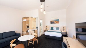 A hotel room with a bed, a sofa, a desk, and a chair. There is a small table and a lamp on the desk. - Glenelg Motel (Glenelg North)