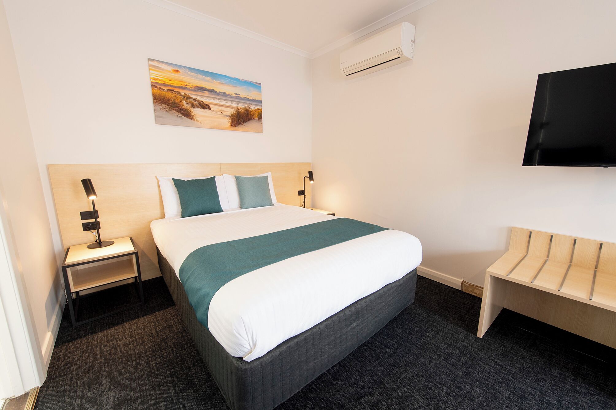 Una camera d'albergo con un letto, un comodino, una TV e una panca.