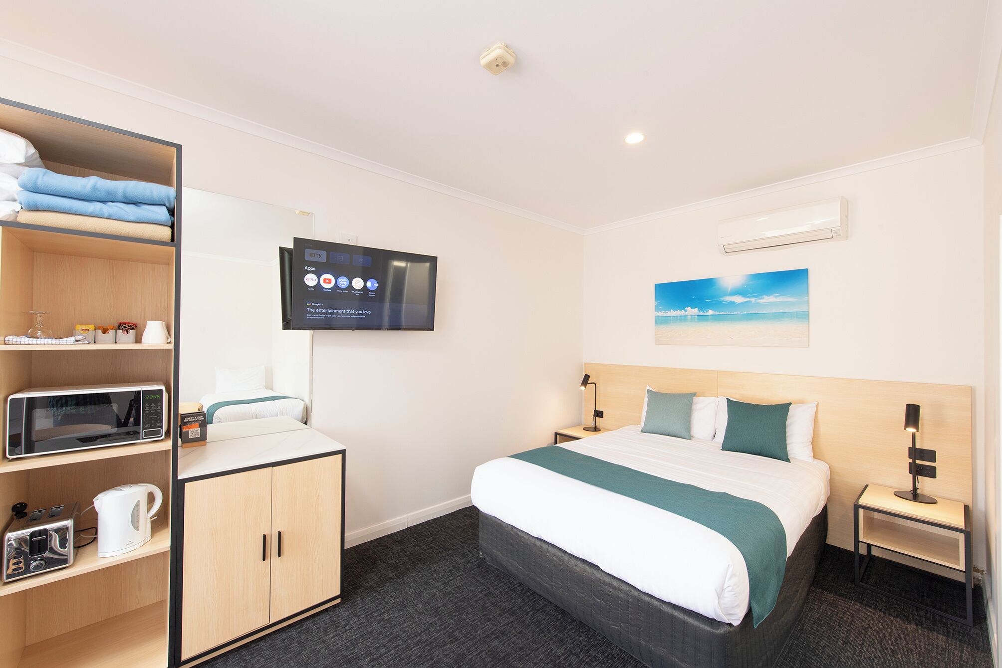 Une chambre d’hôtel équipée d’un lit, d’un téléviseur fixé au mur, d’un four à micro-ondes, d’une bouilloire et d’un petit meuble de rangement.