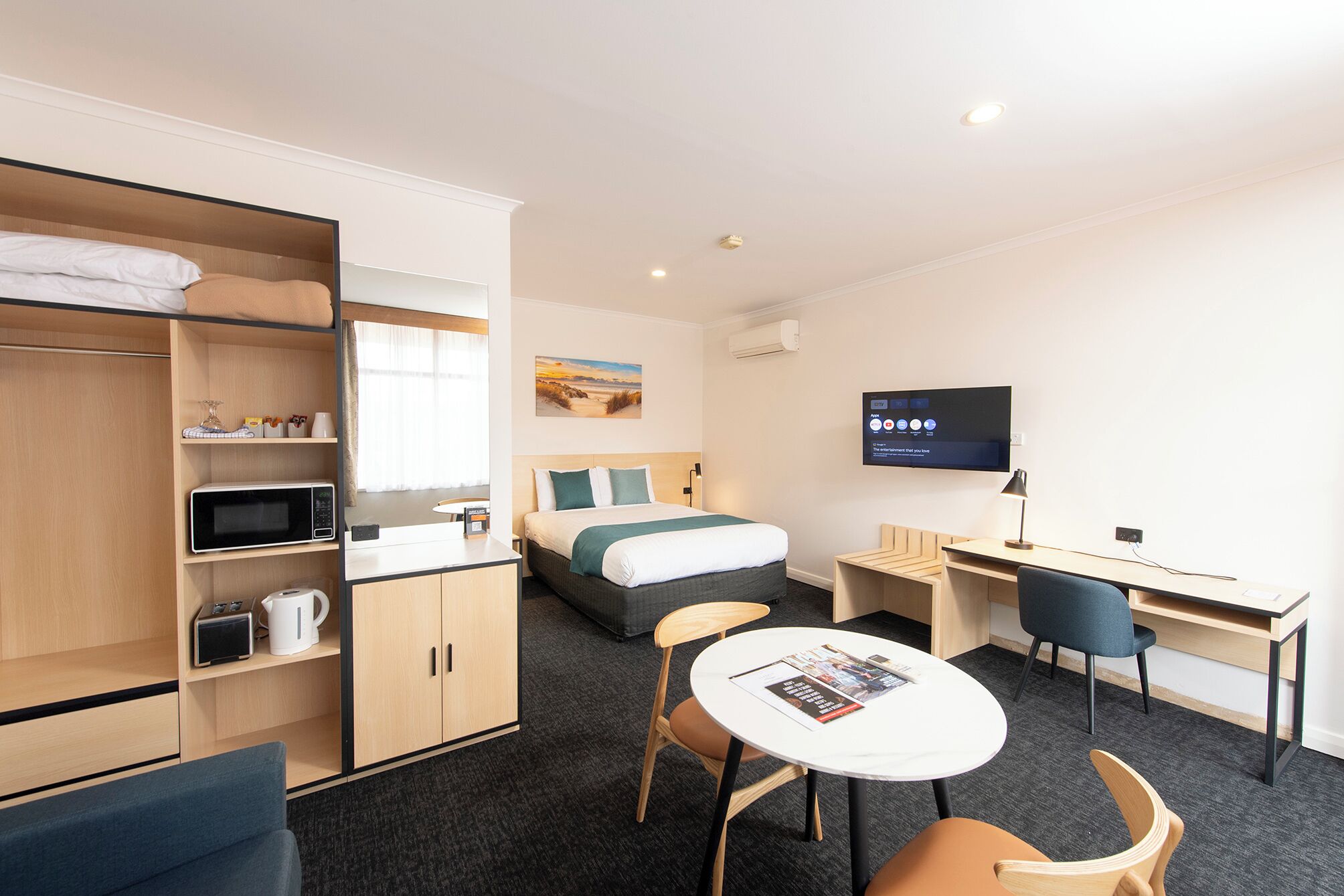 A hotel room with a bed, a desk, a TV, a wardrobe, and a seating area.