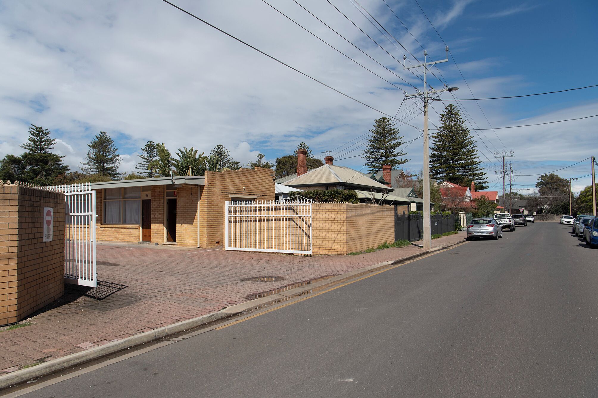 A street view with a gated entrance to a building, a clear sky, and parked cars.