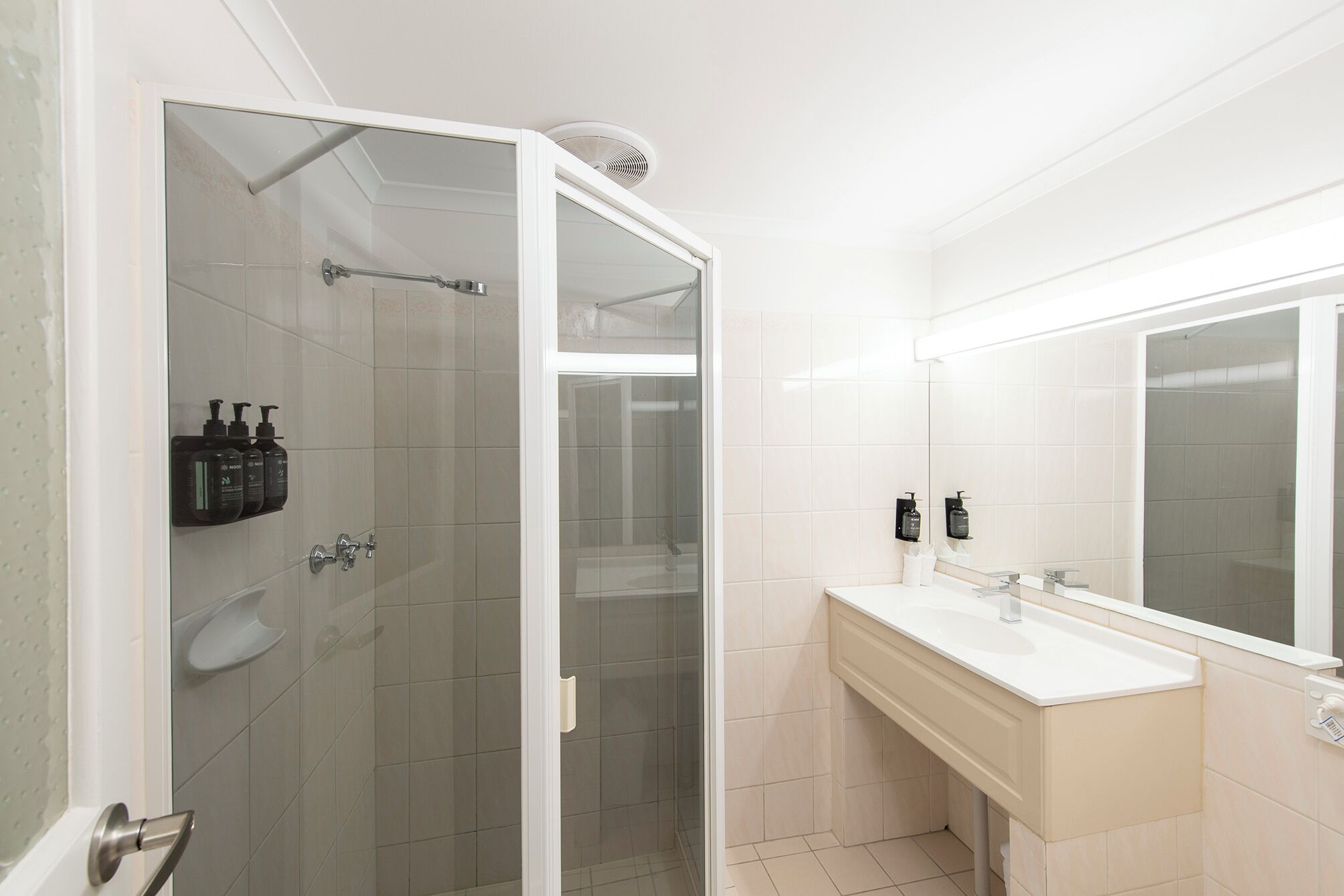 A modern bathroom with a glass-enclosed shower, a white vanity with a mirror, and toiletries on the wall.