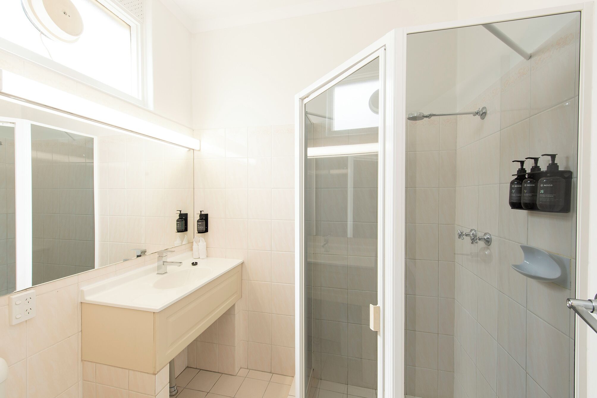 Un baño moderno con tocador blanco, cabina de ducha de vidrio y espejo sobre el lavabo.