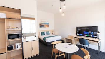 Habitación de hotel con cama, escritorio con televisor, mesa de comedor con sillas, microondas, hervidor de agua y estante con hervidor y tostadora.