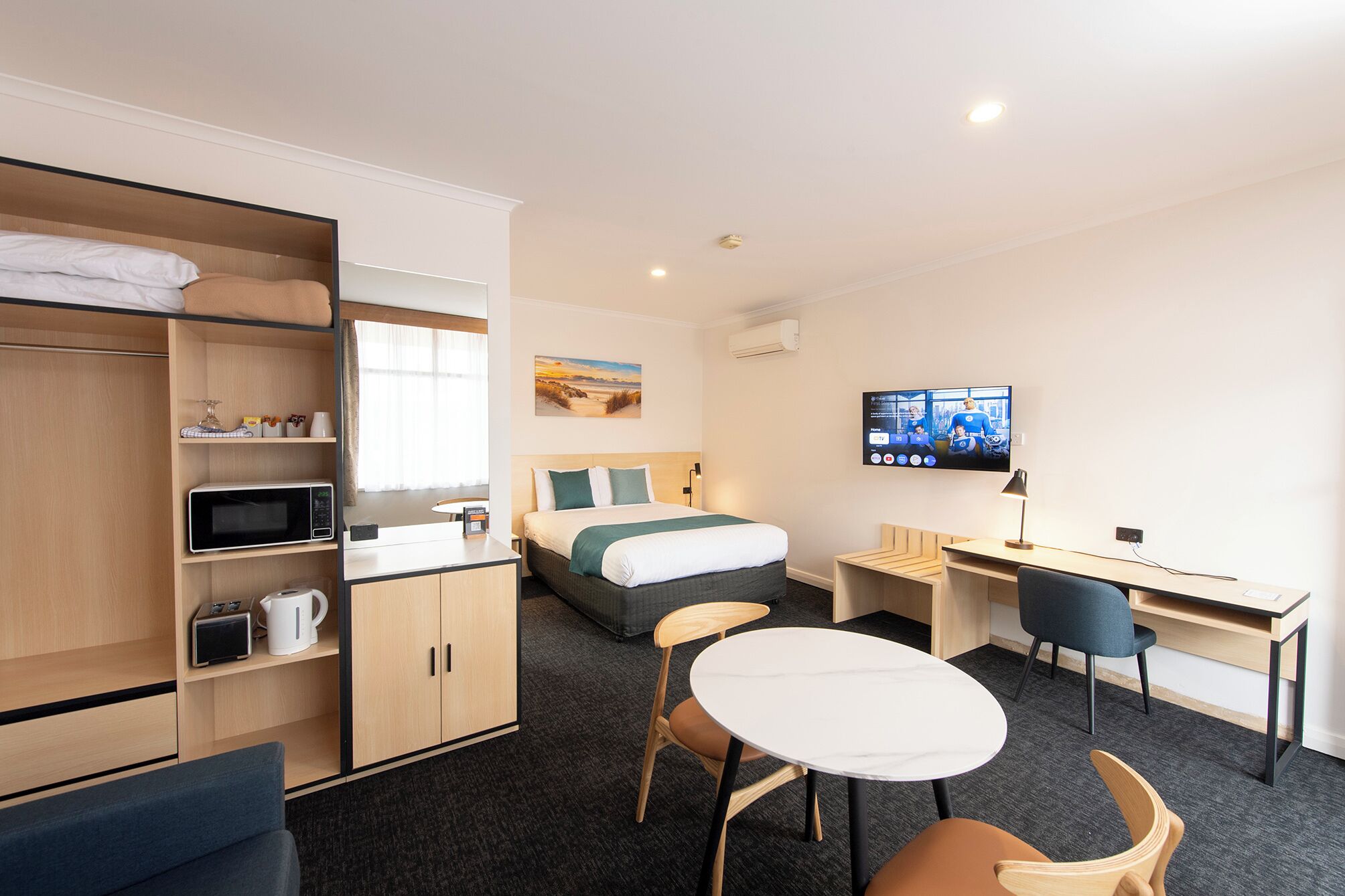 A hotel room with a bed, a desk, a TV, and a seating area.