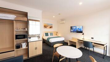 A hotel room with a bed, a desk, a TV, and a seating area.