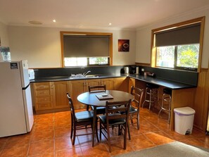 A compact kitchen with wooden cabinets, a dining table with chairs, a sink, and a trash bin. - Abs by the Bay (Taranna)