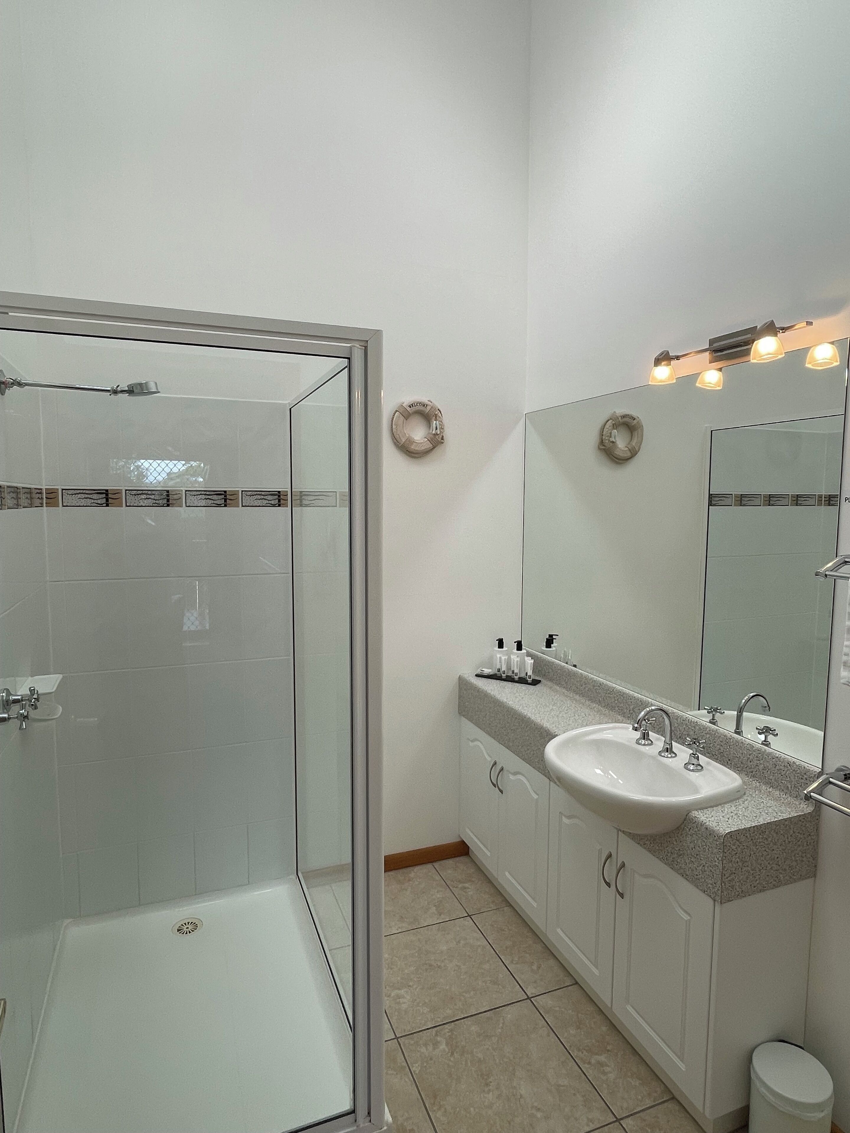 A bathroom with a glass-enclosed shower, a sink with a vanity, and a mirror with lights.
