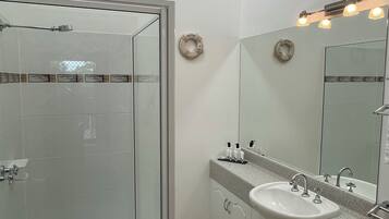 A bathroom with a glass-enclosed shower, a sink with a vanity, and a mirror with lights.