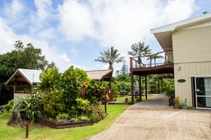 Um edifício com área externa coberta, um jardim com diversas plantas e um caminho que leva à entrada.