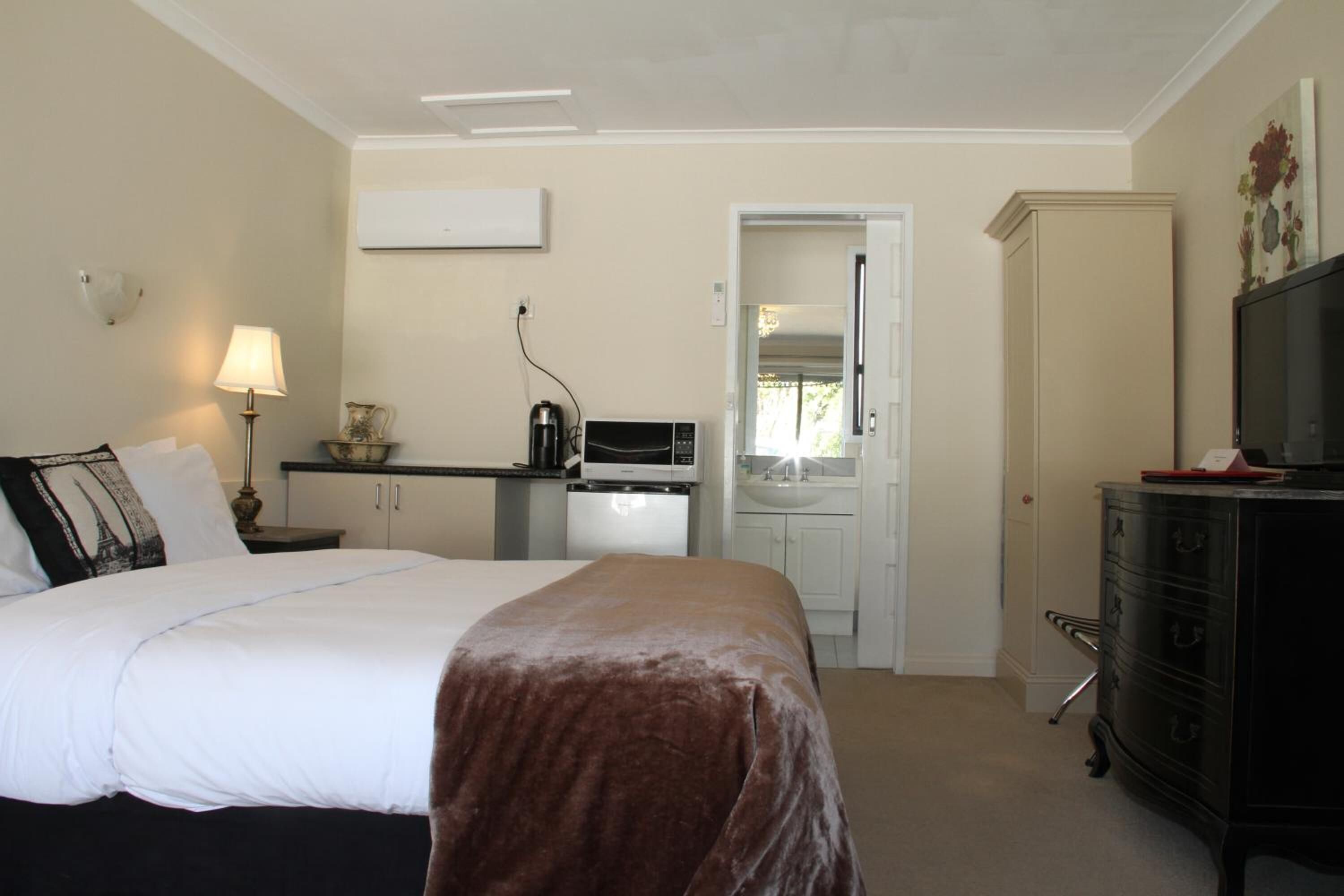 Una habitación de hotel con una cama, un escritorio con microondas, un aparador y un televisor.