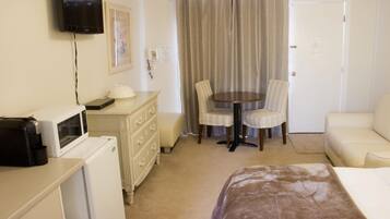 A hotel room with a bed, a desk with a microwave, a dresser, a television, a dining table with chairs, and a door.