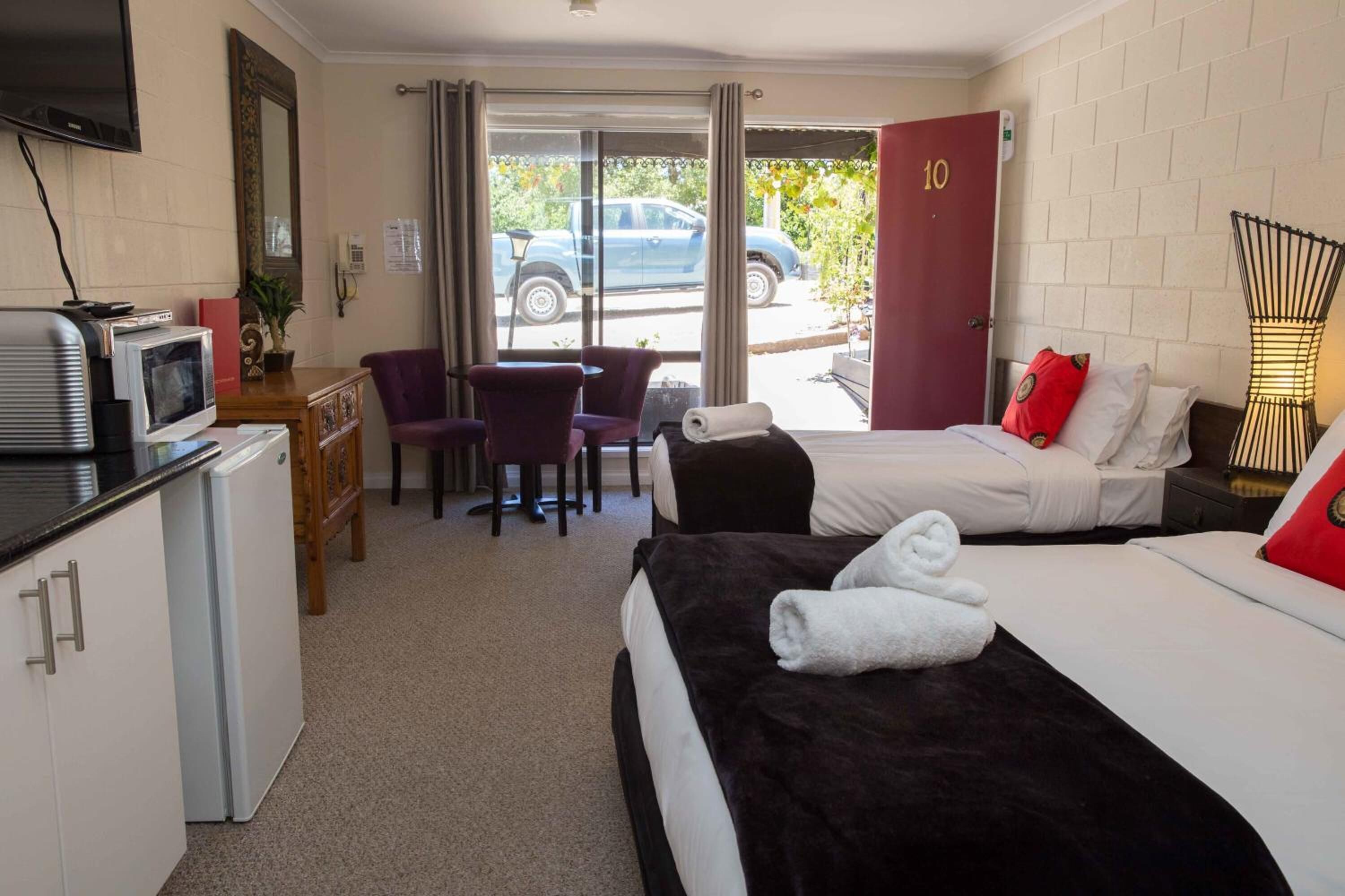 A hotel room with two beds, a desk with a chair, a television, and a small kitchenette.