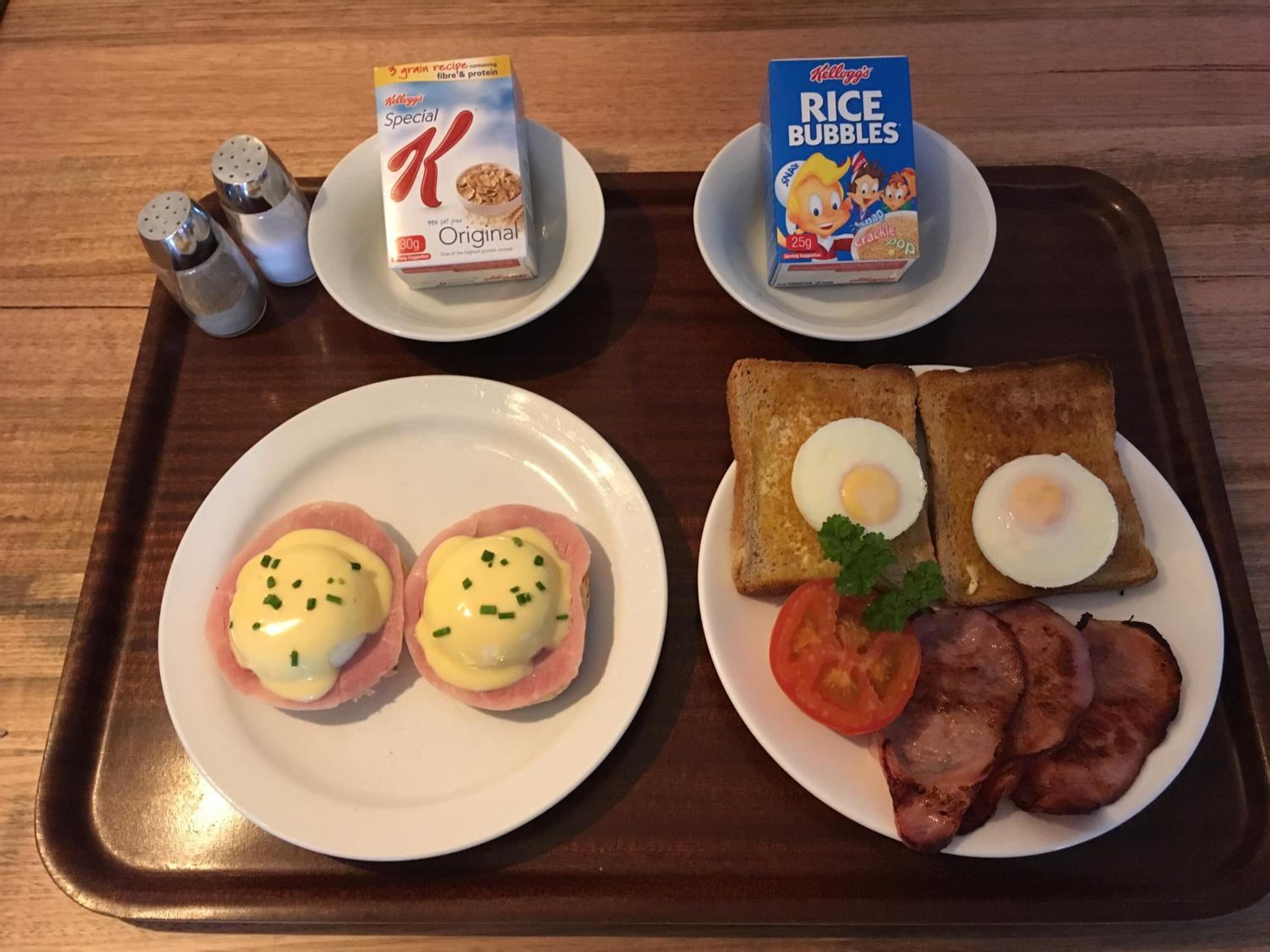 A tray with breakfast items including eggs benedict, toast with eggs, bacon, and cereal boxes.