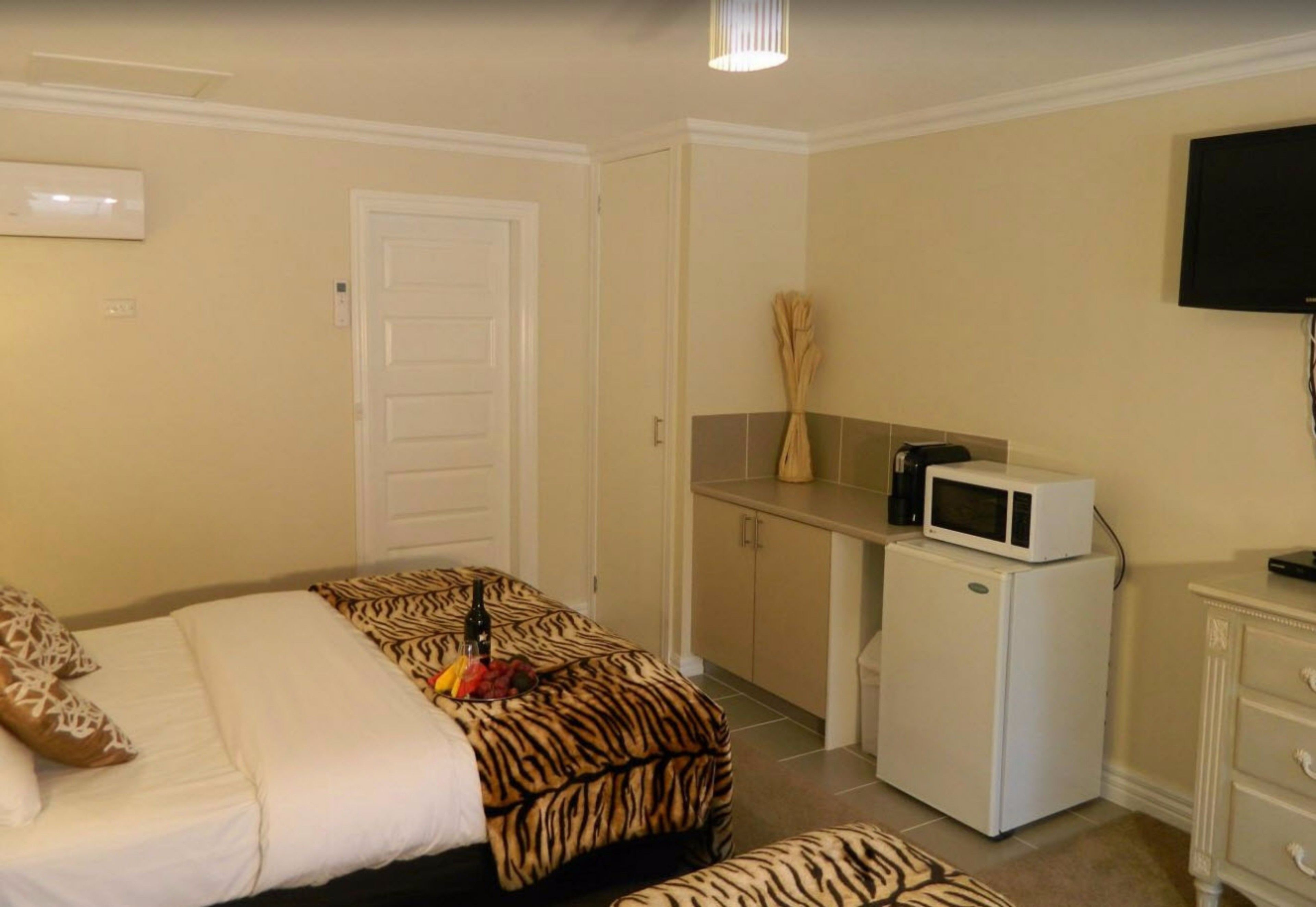 A compact hotel room with a bed, a small kitchenette, a television, and a door.