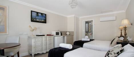 A hotel room with two beds, a dining table, a white dresser, a television, and a chandelier.