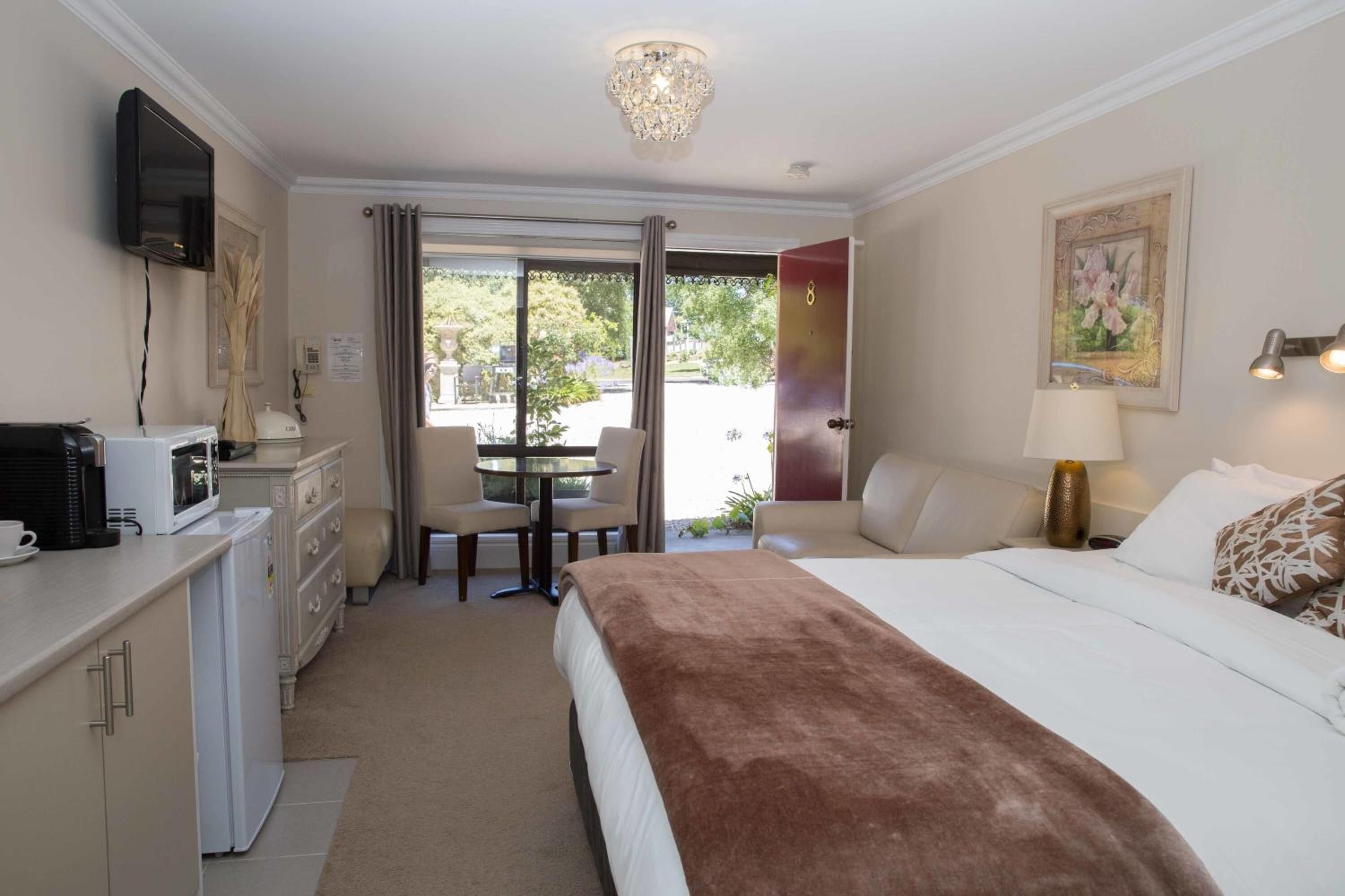 Une chambre d’hôtel comprenant un lit, un bureau avec un micro-ondes, une chaise, une table avec une chaise, un téléviseur fixé au mur et une porte donnant sur un balcon.