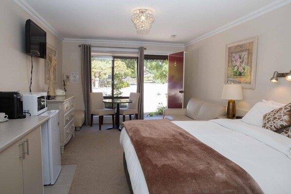 Habitación de hotel con cama, escritorio con microondas, silla, mesa con silla, televisor montado en la pared y puerta que da a un balcón.