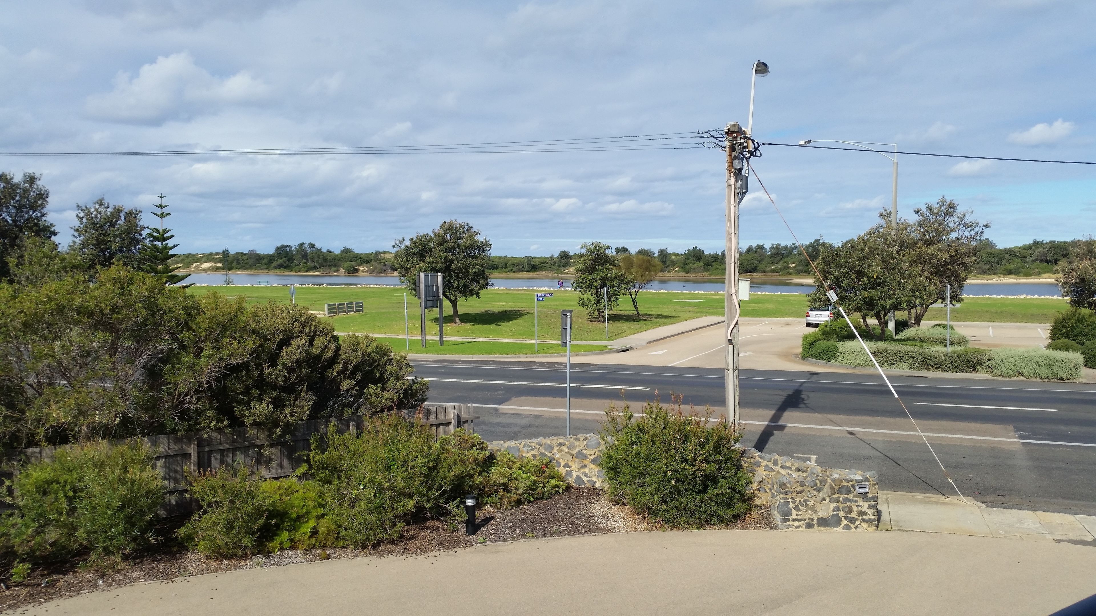 A road intersection with a stone wall, a grassy area, and a body of water in the background.