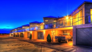 A hotel with multiple floors, a covered outdoor area, and a truck parked in front. - Ultimate Holiday Apartments (Lakes Entrance)