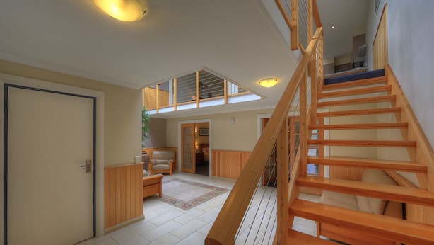 A spacious interior with a wooden staircase, a high ceiling, and a view through a skylight. - Ultimate Holiday Apartments (Lakes Entrance)