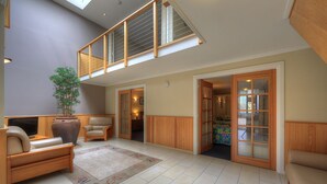 A spacious living area with a high ceiling, a large window, and a built-in bookshelf. - Ultimate Holiday Apartments (Lakes Entrance)